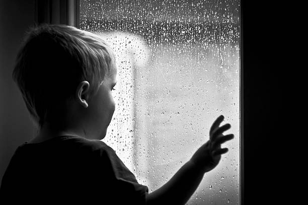 Small boy looking out of a rainy window